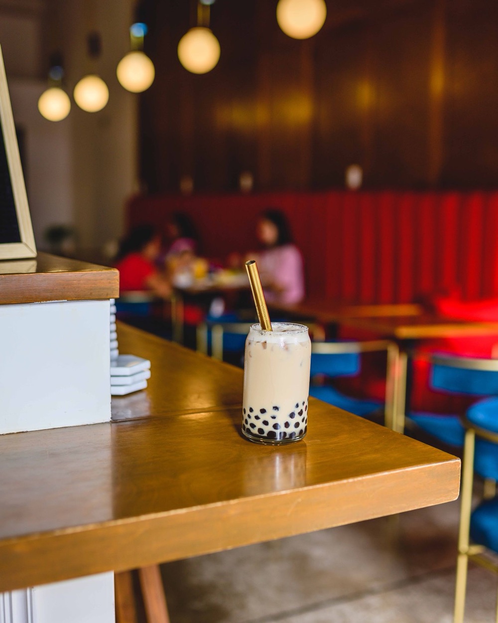 A cup of milk tea with tapioca pearls on a wooden counter in a café with red seating